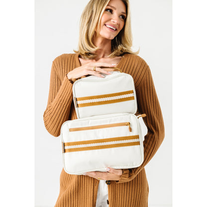 A woman in a brown ribbed cardigan holds two white diaper pail bags with mustard yellow and white stripes against a plain white background.