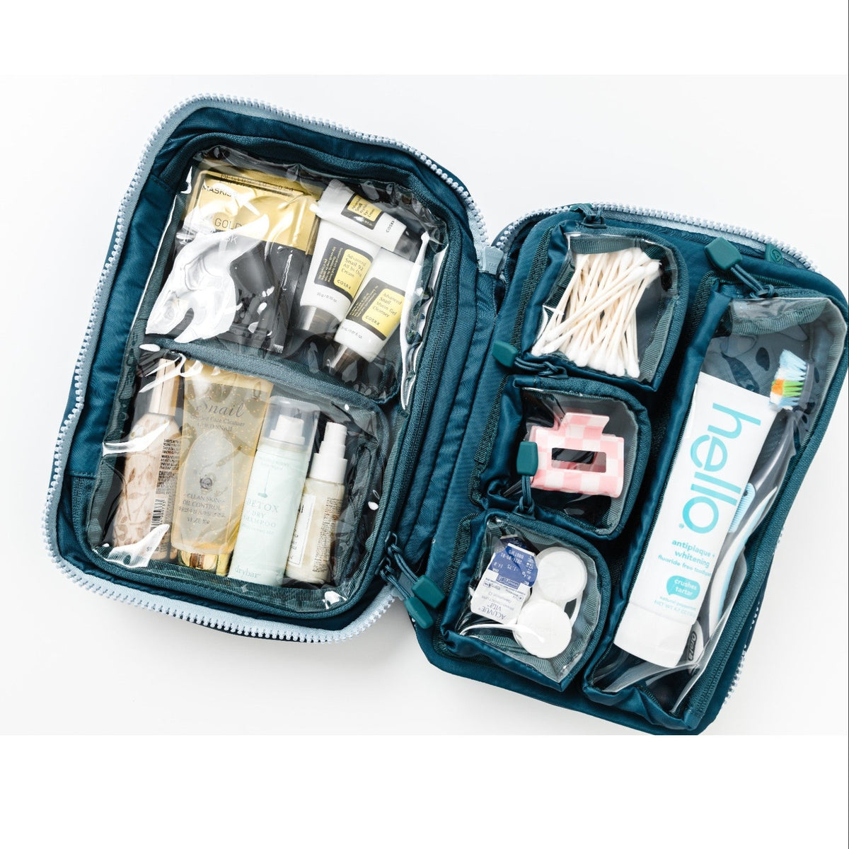 An open teal blue toiletry and first-aid kit organizer filled with various personal care items, including cotton swabs, a pink hair tie, a toothbrush,with hello toothpaste and skincare products, shown on a white background.