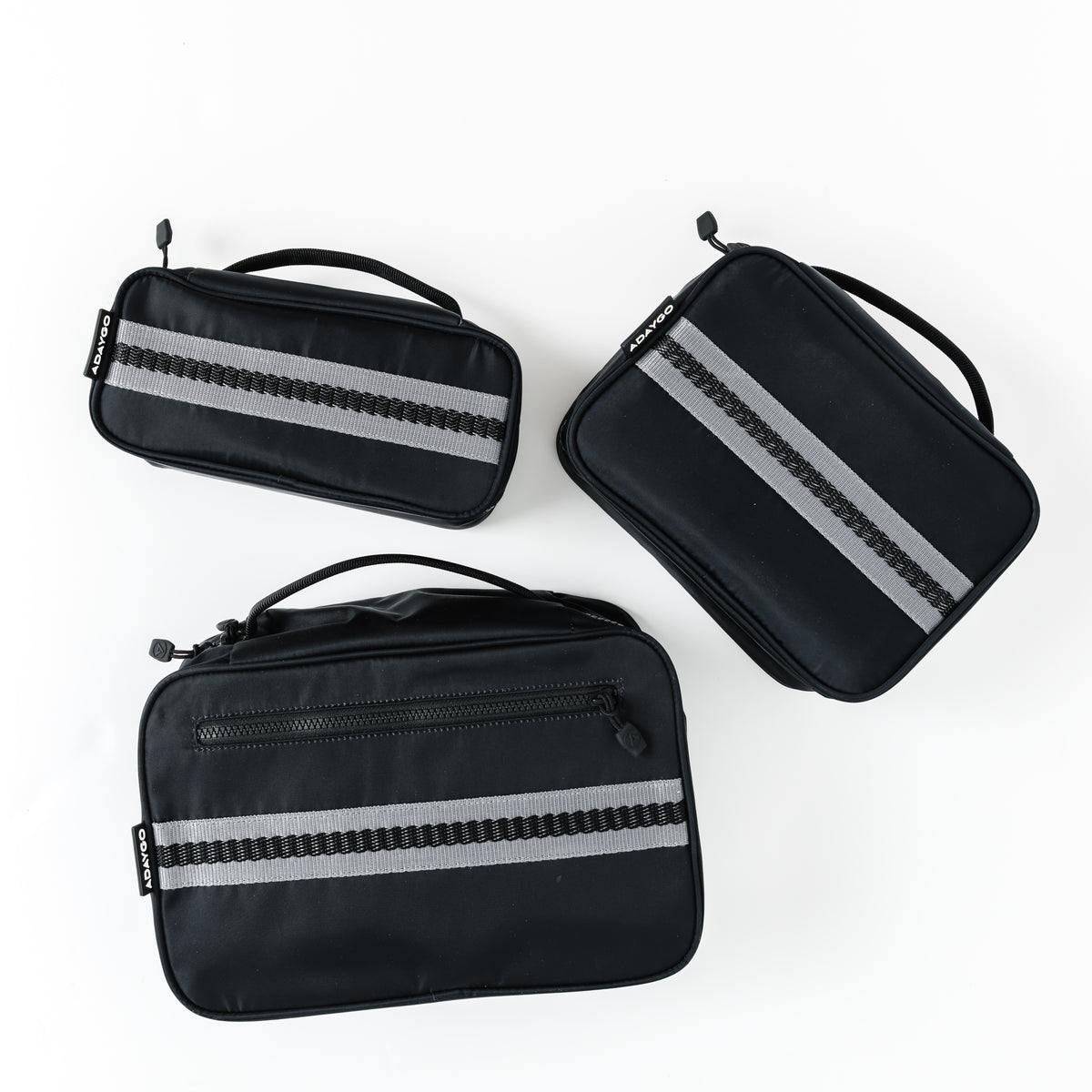 Three black rectangular travel pouches with reflective silver-gray horizontal stripes, arranged on a clean white background.