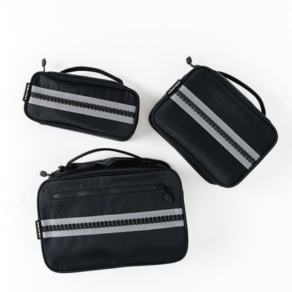 Three black rectangular travel pouches with reflective silver-gray horizontal stripes, arranged on a clean white background.